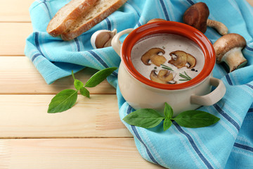 Mushroom soup in pot, on napkin,  on wooden background