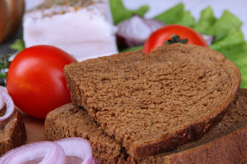 Slices of bread and lard with vegetables on table close up