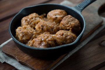 Meatballs with gravy in a frying pan, rustic wooden background