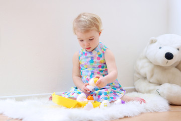 Cute toddler girl playing indoors sorting colorful plastic eggs