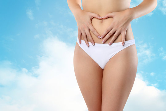 Woman's hands on stomach on sky background wellness concept