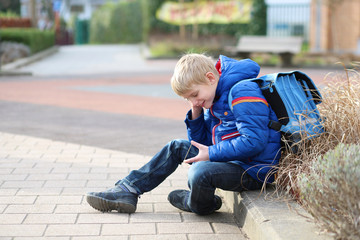 Teenager boy calling on mobile phone sitting outside of school