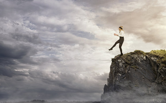 Risk, young businesswoman walking over the edge of the cliff