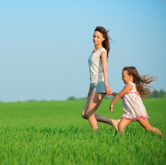 Young happy girls running at green wheat field