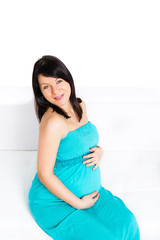 Beautiful, pregnant woman sitting on sofa and looking at camera