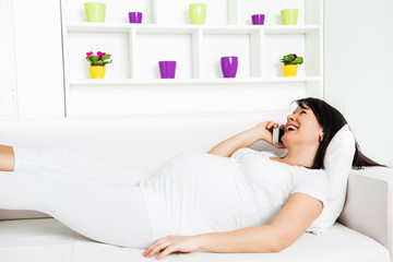 Beautiful pregnant woman lying on sofa and using a mobile phone