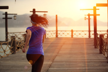 back of fitness woman runner running at wooden pier