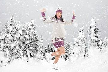Happy pregnant woman dancing in the snowy forest