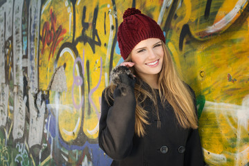 Cute blonde teenage girl with hat against graffiti wall