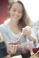 beautiful young woman spreading jam on bread focus on hands in f