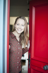 beautiful young woman opening a red door to welcome someone