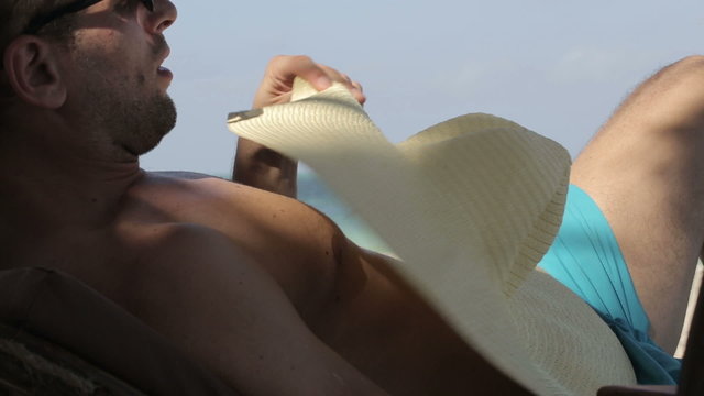 Man on sunbed colling himself with hat