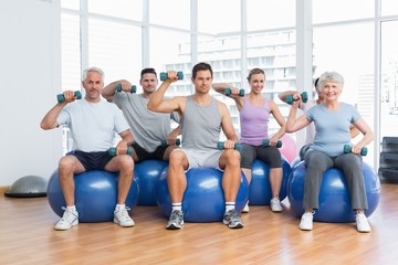 Fototapeta premium Fitness class with dumbbells sitting on exercise balls in gym