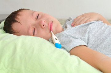 Obraz na płótnie Canvas Boy with a thermometer in his mouth lying in bed