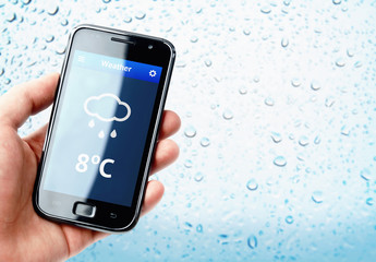 Hand holding smartphone with weather with rainy window