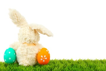 Toy Easter bunny on grass with colorful eggs
