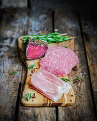 Sliced prosciutto di Parma on wooden board with salami and rosem