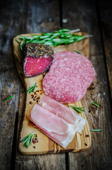 Sliced prosciutto di Parma on wooden board with salami and rosem