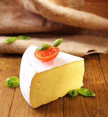 Tasty Camembert cheese with tomato and basil, on wooden table