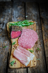 Sliced prosciutto di Parma on wooden board with salami and rosem
