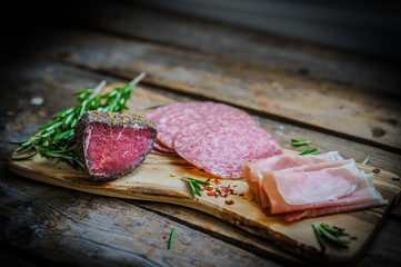 Sliced prosciutto di Parma on wooden board with salami and rosem