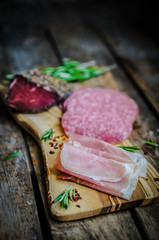 Sliced prosciutto di Parma on wooden board with salami and rosem