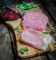 Sliced prosciutto di Parma on wooden board with salami and rosem