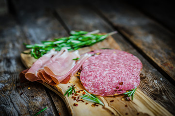 Sliced prosciutto di Parma on wooden board with salami and rosem