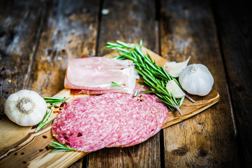 Sliced prosciutto di Parma on wooden board with salami and rosem