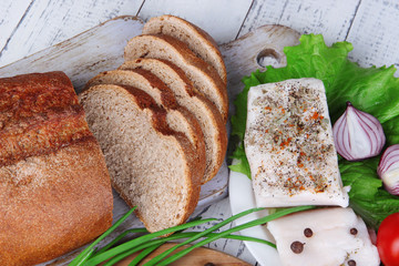 Slices of bread and lard with vegetables on table close up