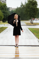 Happy woman with umbrella walking on the rainy city street