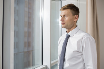 Fototapeta premium Thoughtful mid adult businessman looking through window at home