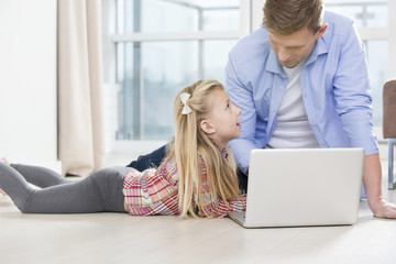 Father and daughter using laptop on floor in living room