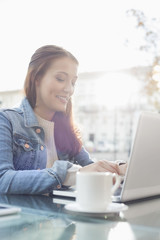 Smiling young woman using laptop at sidewalk cafe