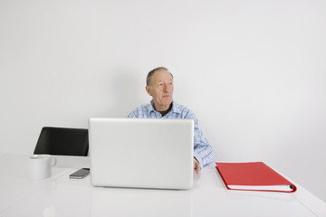 Thoughtful senior businessman using laptop at office desk