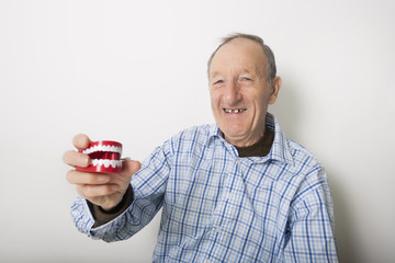 Portrait of smiling senior man holding teeth model against gray background