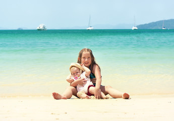 Fototapeta na wymiar Two happy smiling sisters sitting on a tropical beach.