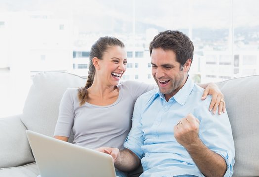 Excited Couple Sitting On The Sofa Using Laptop Together