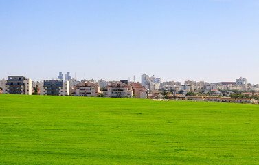 Fototapeta na wymiar Beer Sheva suburb behind a green field under blue sky