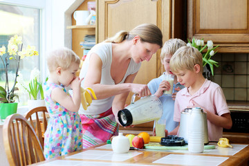 Mother with kids preparing healthy drink with milk and fruits