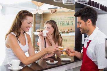 Barista giving pastry to woman at counter in coffee shop