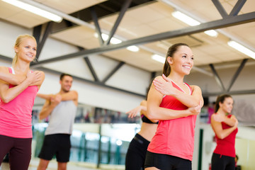 Fototapeta na wymiar group of smiling people stretching in the gym