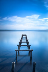 Wooden pier or jetty remains on a blue lake. Long Exposure.