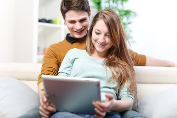 Young couple using digital tablet indoors on the sofa