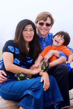 Mutiracial family with disabled son sitting on beach on misty da