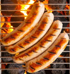 Gardinen Four sausages called bratwurst, grilling over hot coals on a BBQ © exclusive-design
