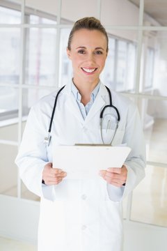 Happy beautiful female doctor with clipboard in hospital