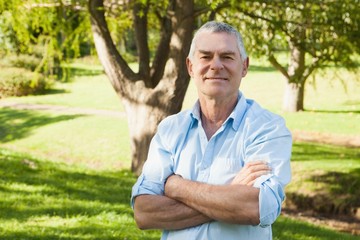 Content mature man with arms crossed at park