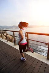 Foto auf Acrylglas Joggen Fitness-Frau, die auf der Holzbrücke am Meer läuft