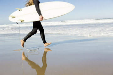 Teenage girl running on the beach with her surfboard
